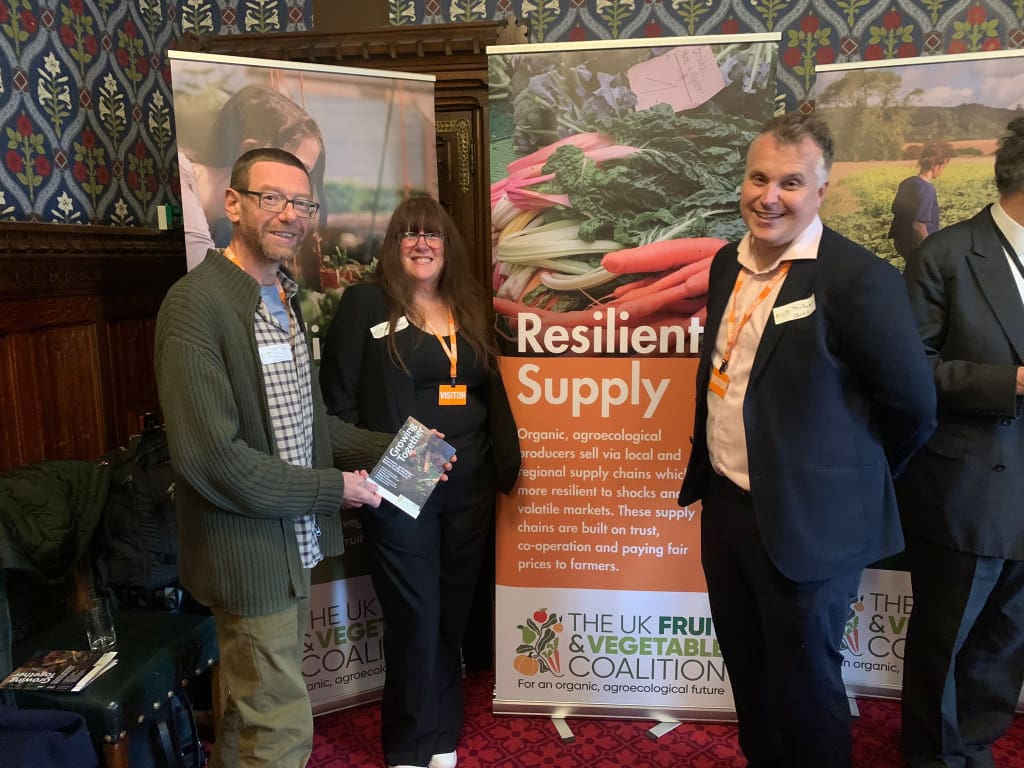 Three people stand in front of roll-up banners in panelled room with a policy pamphlet