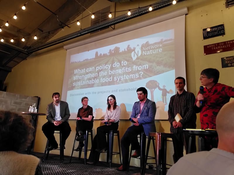 Six people on stage as part of a panel discussion with slide behind