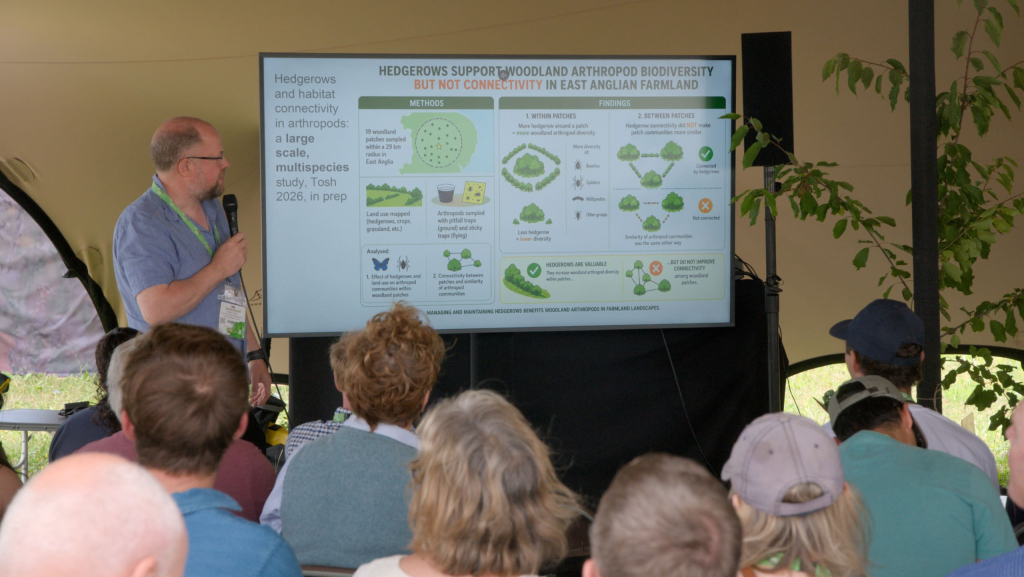 Colin in front of screen with slide and audience in a tent