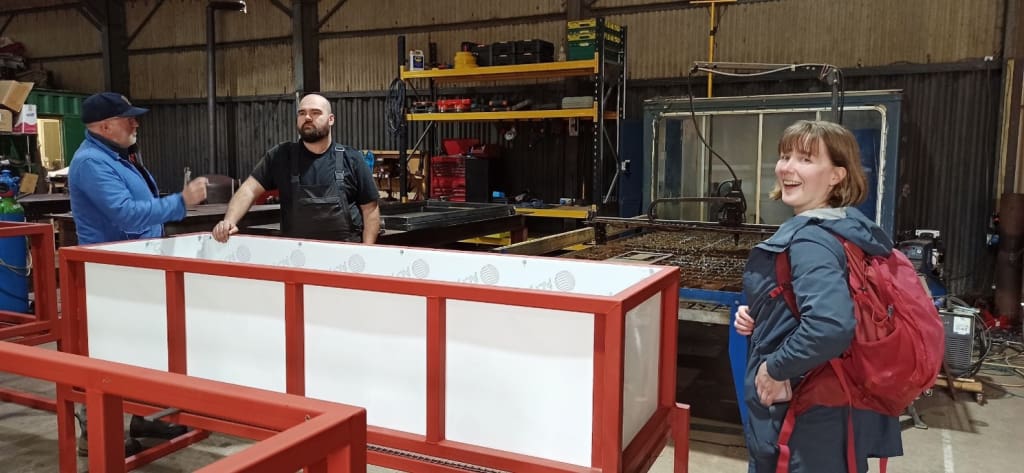 3 people standing around one of the vermoicomposting bins in the barn